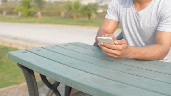 Young Man Using Phone, while Sitting in Park