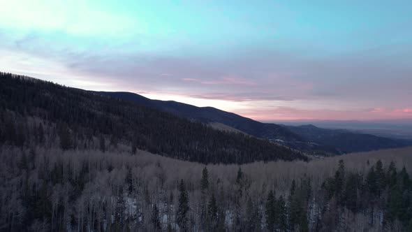 A drone shot over top of a mountain peak with forest and sunrise