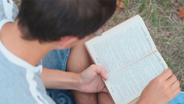 Man is Reading a Book Outdoors