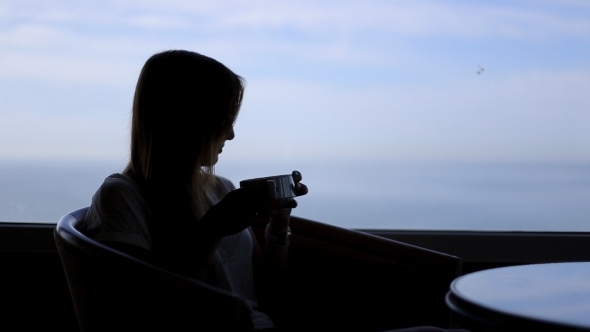 Silhouette Of Young Beautiful Woman Sits In a Cafe