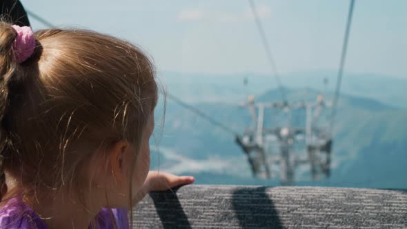 Cute Girl Rides Ropeway Sitting on Soft Bench in Gondola