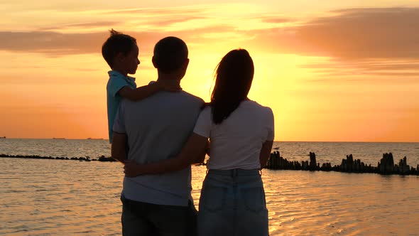 A Happy Family Stands on the Beach and Enjoys a Beautiful Sunset. A Father Holds His Son in His Arms