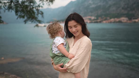 Loving Tender Asian American Young Mum Holding Adorable Cute Baby Boy Daughter Embracing Kissing