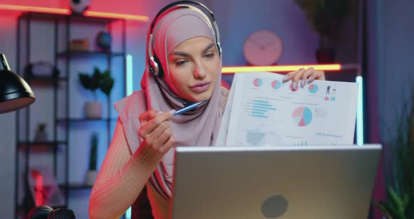 Woman in Hijab Explaining Charts Via Video Meeting on Laptop Sitting in Home Office