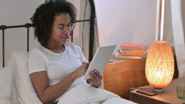 Young African Woman Celebrating Success on Tablet in Bed 