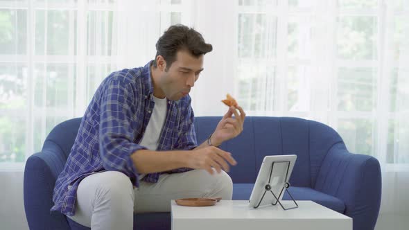 Caucasian man at home eating slice of pizza online together with her girlfriend in video conference