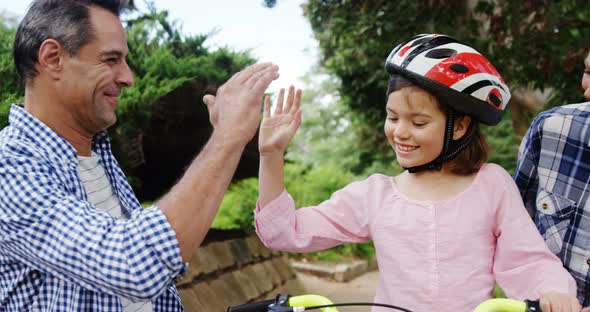 Girl sitting on a bike while happy parents giving high five and hugging her