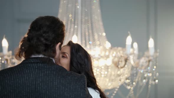 Happy Brunette Woman is Kissing His Beloved Man and Looking at Camera Coquettishly