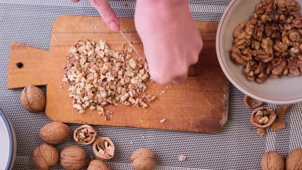 Chopping Walnuts Cores with Kitchen Knife on a Wood Cutting Board