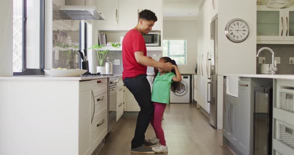 Happy biracial father and daughter dancing in kitchen together