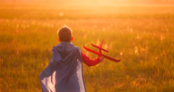 The Boy Runs Across the Field with a Plane in His Hands at Sunset