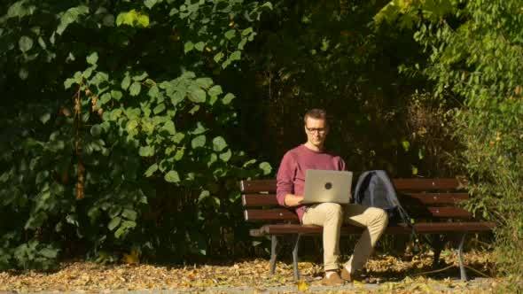 Man in Glasses is Sitting on The Bench Working