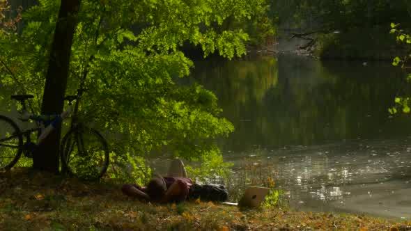 Man is Sitting at Lake Bank Working With Laptop