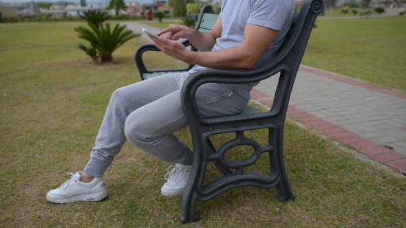 Young Man Using Smartphone, Sitting on Bench