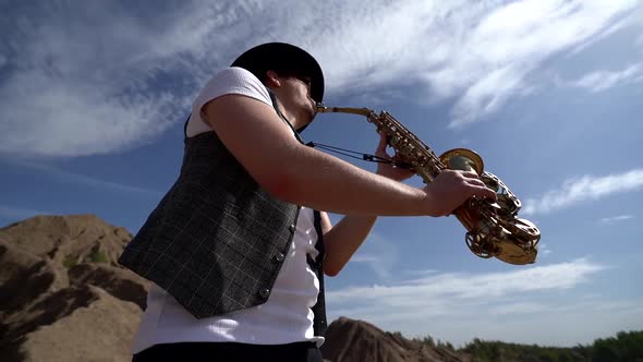 Portait Musician in a Hat Plays Jazz on a Saxophone, Standing in the Desert Against the Background