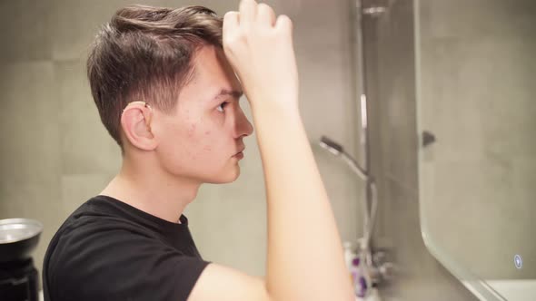 Pimply Guy in Hearing Aids Styling His Hair Against the Background of an Old Wall