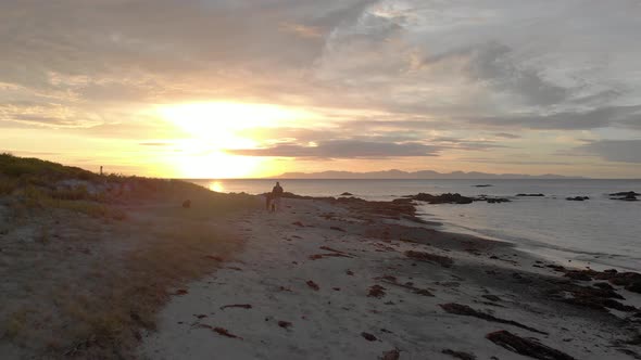 A forward moving aerial shot of a father and children on a sandy beach with a beautiful sunrise on t