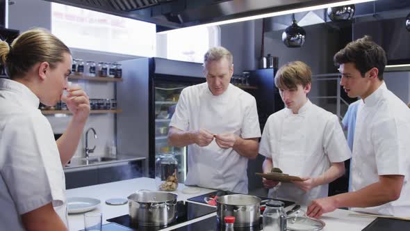 Professional Caucasian male chef in a restaurant kitchen teaching male trainee chefs