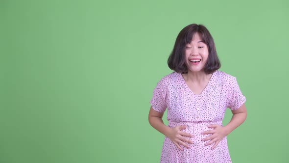 Happy Asian Pregnant Woman Pointing Up and Looking Surprised