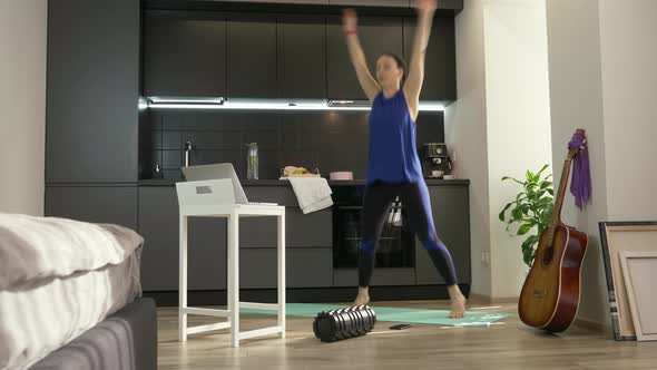 Woman jumping and doing fitness aerobic exercises at home in kitchen using online training app