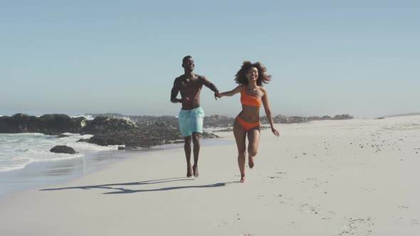 African American couple running side by side at beach