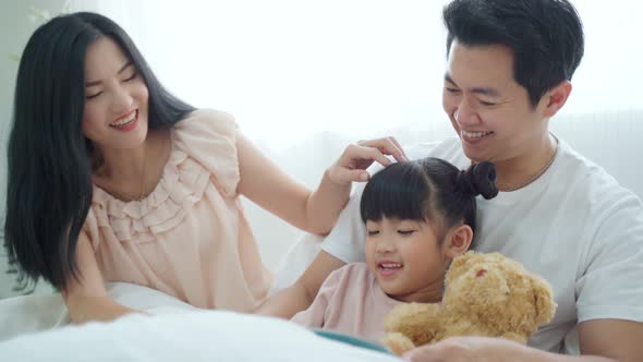 Happy Asian family, Parents spend leisure time with young little kid daughter in bedroom at house.