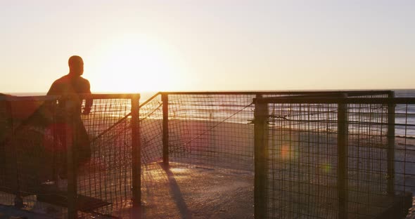 Focused african american man running up stairs, exercising outdoors by seaside at sunset