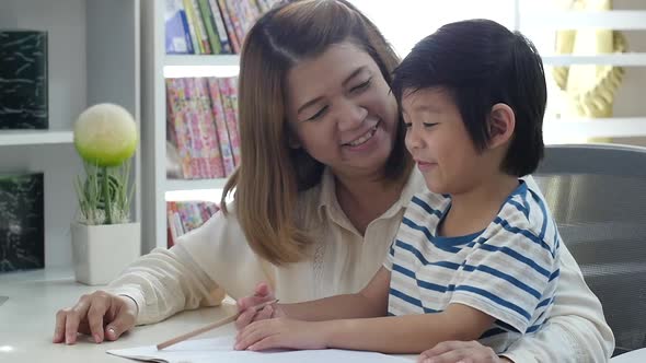 Asian Mother Helping Her Son Doing Homework On White Table