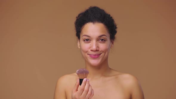 Beauty Portrait of Young African American Woman Blowing Off Powder Particles From Makeup Brush