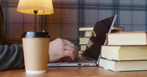 Male Hands During Work in Front of a Laptop Monitor in a Library in the Light of a Table Lamp