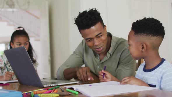 African american father, daugher and son sitting at kitchen table doing homework