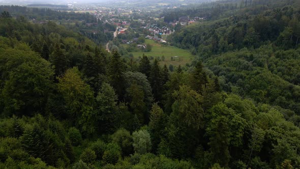 Aerial drone view low over mountain forest towards a village overcast in Ukraine