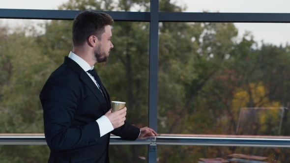 Young Businessman Drinking Coffee At Office Window