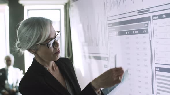 Confident Businesswoman Checking Papers with Data on Screen