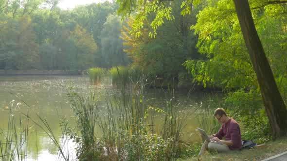 Man in Glasses is Sitting at the Lake Bank