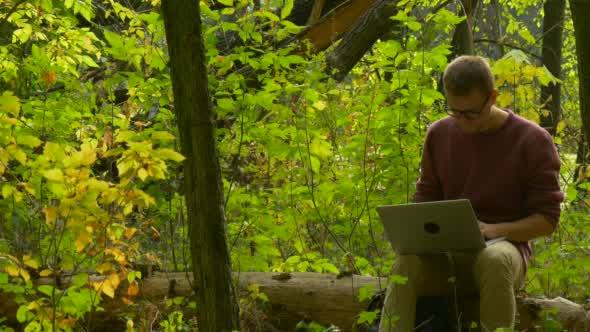 Man in Glasses is Sitting on a Fallen Tree Trunk