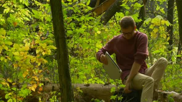 Man in Glasses is Sitting on a Fallen Tree Trunk