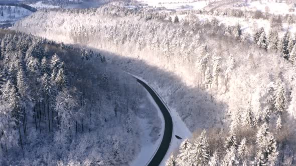 Smooth drone flight over a winterwonderlandscape with an empty road in a valley, flying a little lef