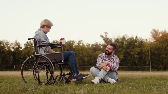 Man is Sitting Next to Disabled Woman in Wheelchair on Field