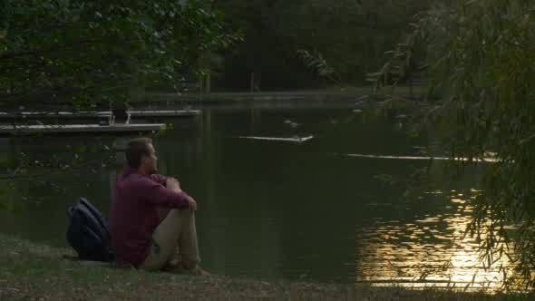 Man is Sitting at The River Lake Bank Backpack is