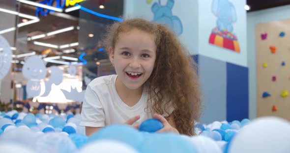 Portrait of a Cheerful Little Girl Smiling Child on Background Children's Plastic Ballskid Looks at
