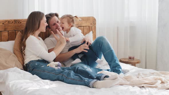 Young Caucasian Parents with Little Daughter Kid Toddler Infant Lying in Cozy Bed Mom Playing Patty