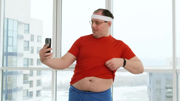 Funny Fat Man with Big Belly Posing and Doing Selfie in Bright Gym or at Home