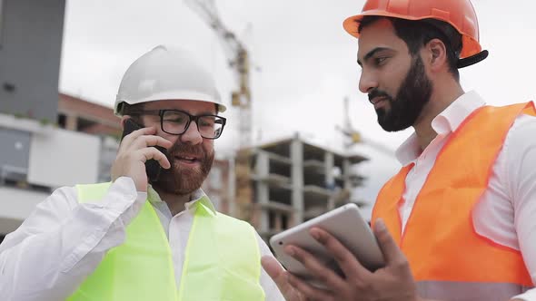 Happy Engineer Speaks on Mobile Phone on Construction Site and Checks the Work of the Worker