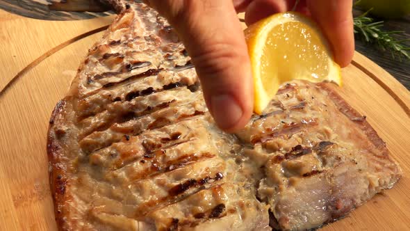 Hand is Squeezing Slowly Lemon Juice on the Grilled White Mackerel Fish Fillet