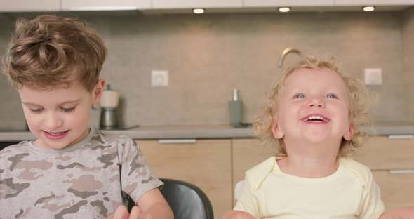 Adorable Brother and Sister Smile and Laugh Together While Sitting at the Kitchen Table Boy Holds