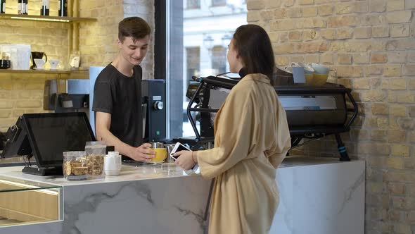 Positive Caucasian Young Bartender Giving Cup of Cappuccino To Beautiful Smiling Woman in Cafe