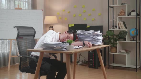 Tired Asian Man Sleeping Due To Working Hard With Documents At The Office