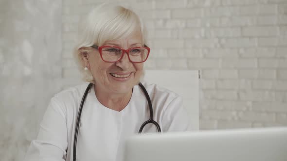 Senior Confident Female Doctor in Eyeglasses Sits in the Cab and Using Laptop for Online