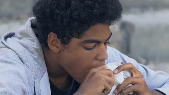 Poor afro-american young male greedily biting burger